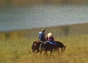 John Denver and Miss Piggy ride horses by a lake in Colorado.