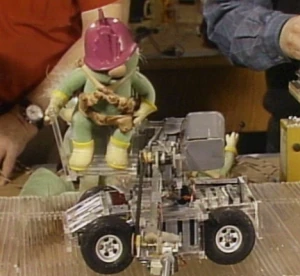 Doozer and vehicle in the Muppet Workshop, with a builder standing nearby.